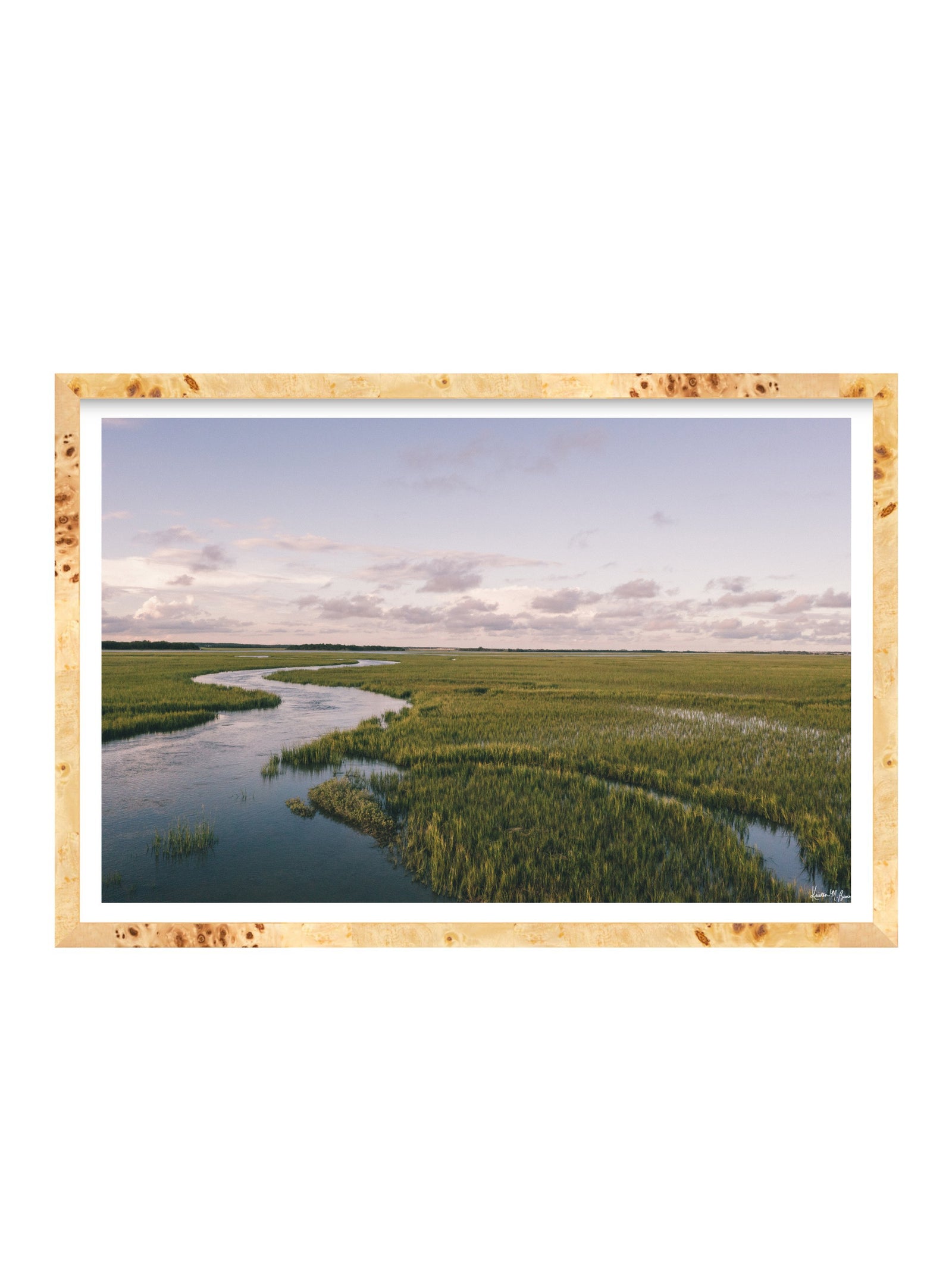 A framed landscape photograph of a winding river through green marshlands under a pale sky, presented in a burlwood frame with a white mat on a white background.