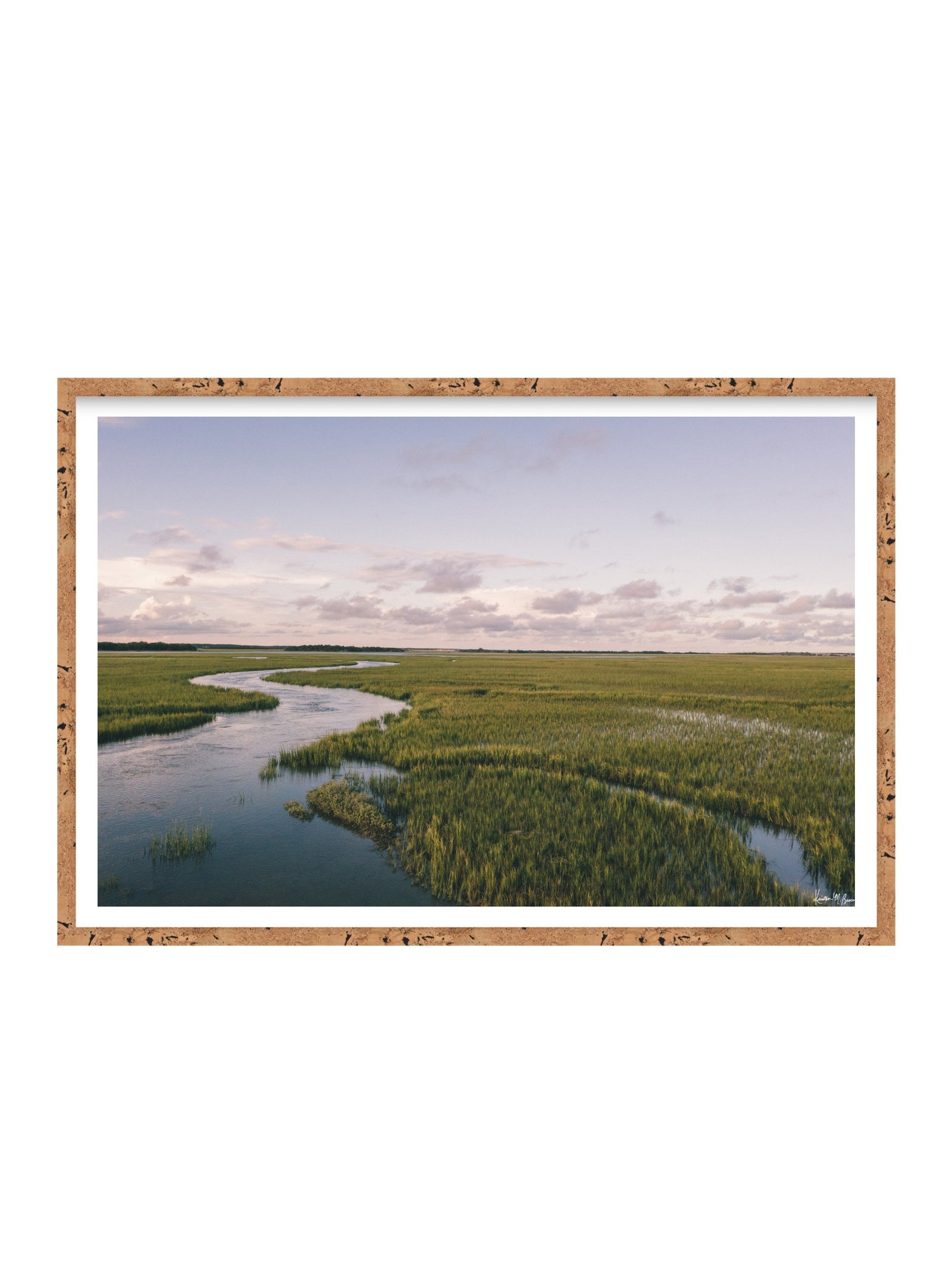 A framed landscape art print depicting a winding river through green marshlands under a pale sky, set in a cork frame with a white mat on a white background. A scenic landscape photograph of a winding river flowing through a vast green marsh under a pale blue and pink sky. "Creek Serenade" photo print of golden hour over the a marsh wandering creek during high tide in Charleston, SC. Photo by Kristen M. Brown of Samba to the Sea for The Sunset Shop.
