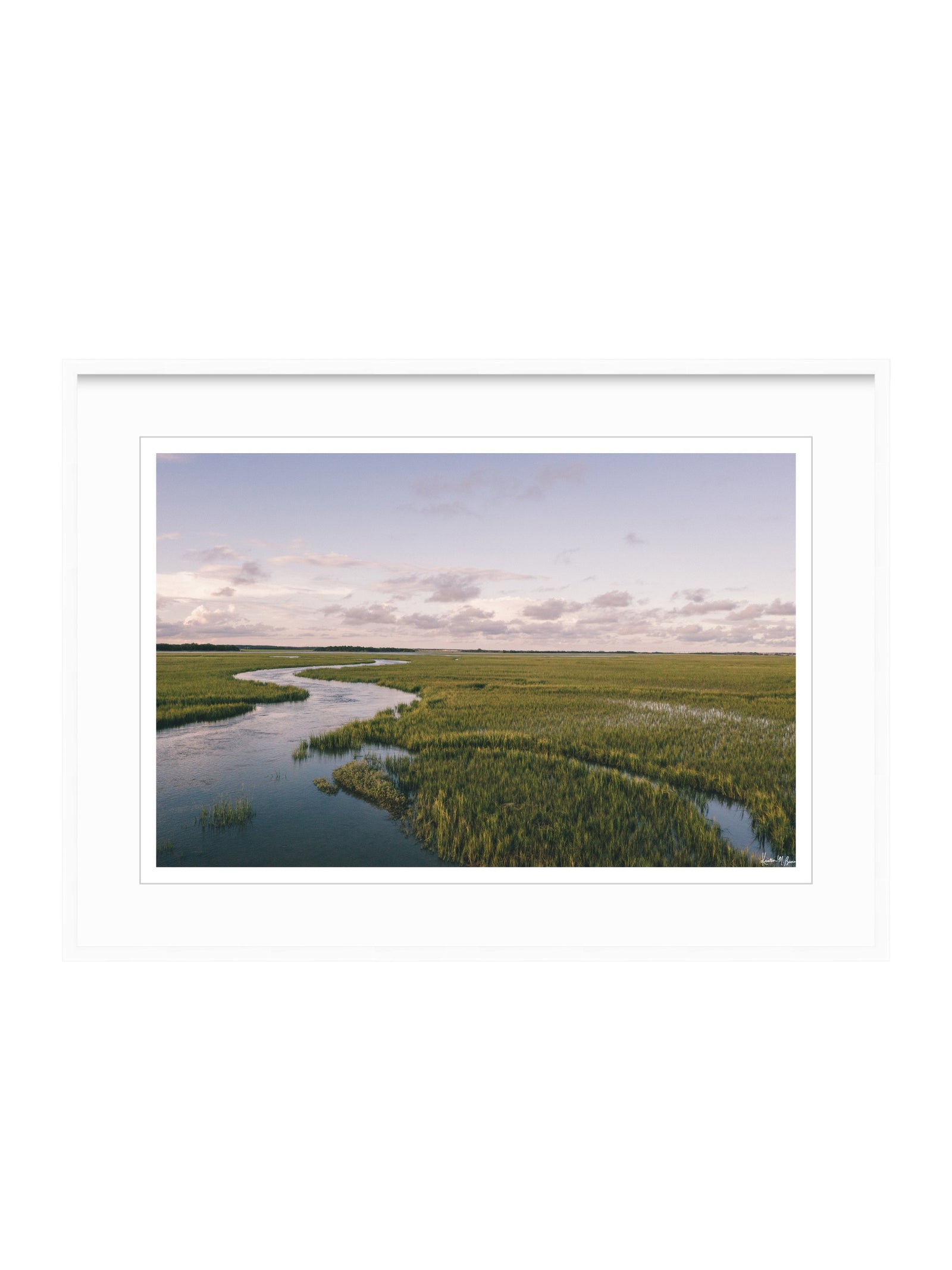 A framed landscape art print depicting a winding river through green marshlands under a soft cloudy sky, presented on a clean white background. A scenic landscape photograph of a winding river flowing through a vast green marsh under a pale blue and pink sky. "Creek Serenade" photo print of golden hour over the a marsh wandering creek during high tide in Charleston, SC. Photo by Kristen M. Brown of Samba to the Sea for The Sunset Shop.