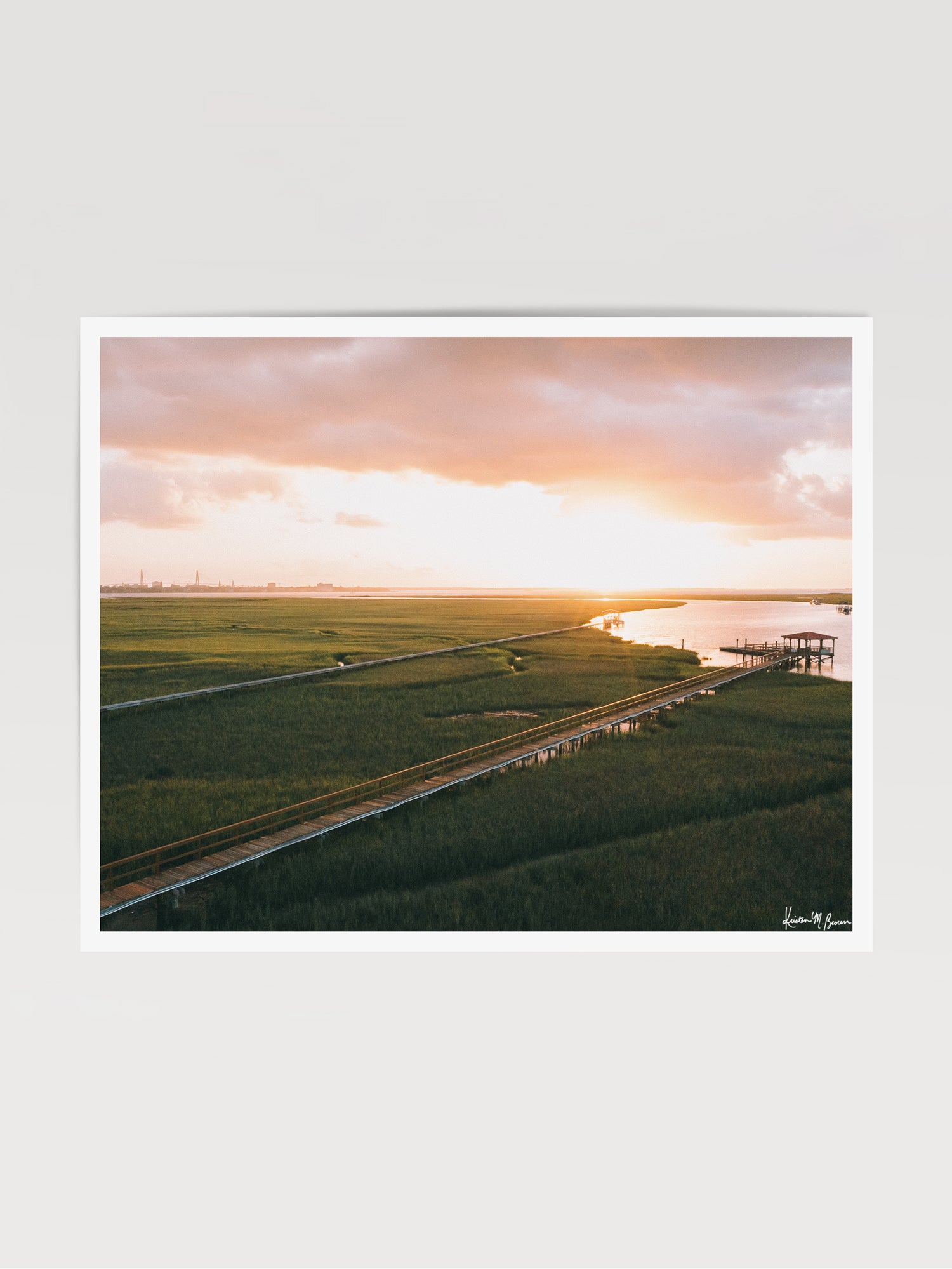 Aerial photograph print of pastel pink sunrise over Charleston harbor and marsh with a boardwalk path, waterway, and view of downtown Charleston in the background. "Morning Harbor View" fine art photography print photographed by Kristen M. Brown, Samba to the Sea.