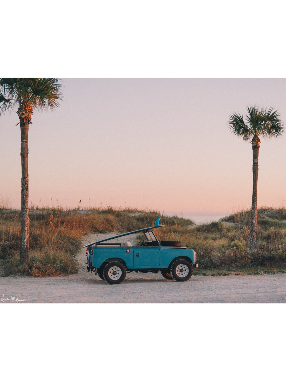 Photograph of vintage Land Rover series truck parked at the beach with a classic single fin surfboard amidst a pastel pink sunset sky. "Wave Chaser" photographed by Kristen M. Brown, Samba to the Sea.