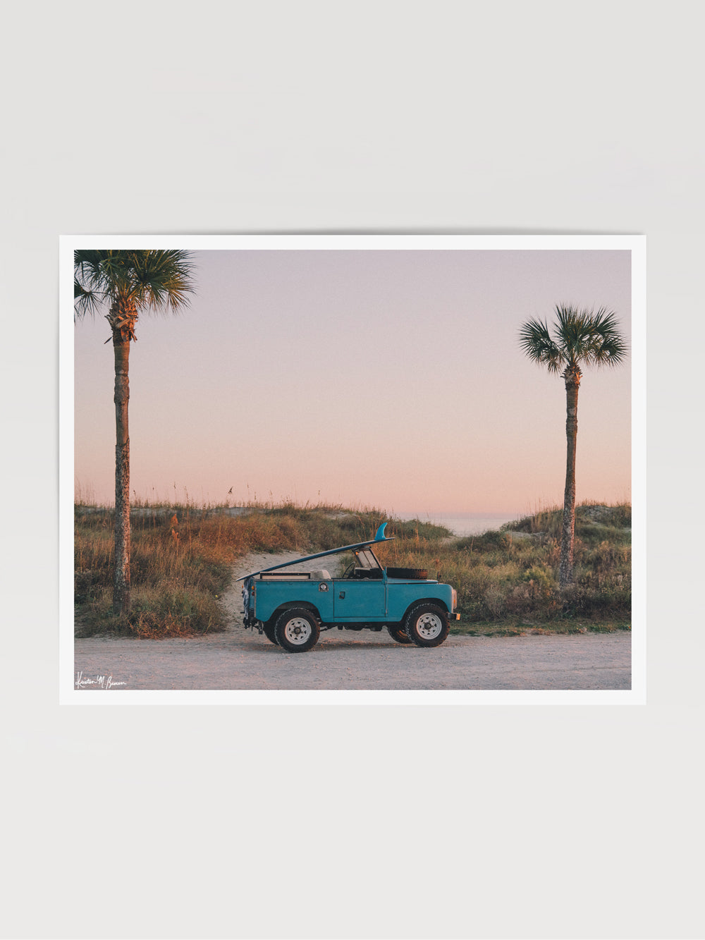 Photograph print of vintage Land Rover series truck parked at the beach with a classic single fin surfboard amidst a pastel pink sunset sky. "Wave Chaser" photographed by Kristen M. Brown, Samba to the Sea.