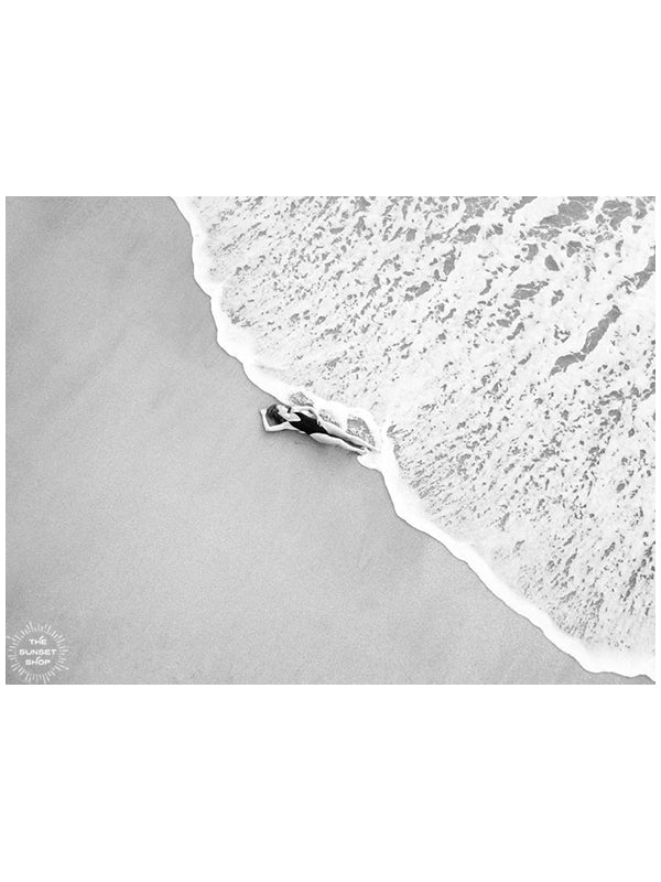 Black and white image of woman laying on the beach as the waves reach her feet in Costa Rica. Photographed by Samba to the Sea for The Sunset Shop.