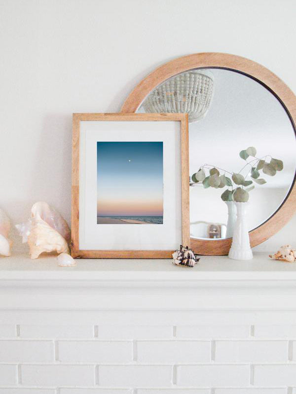 Full moon rising during a pastel sunrise at the beach over the Gulf Coast in Gulf Shores, Alabama. Photographed by Kristen M. Brown, Samba to the Sea for The Sunset Shop. Coastal living framed sunrise beach print shelfie on white fireplace mantle.