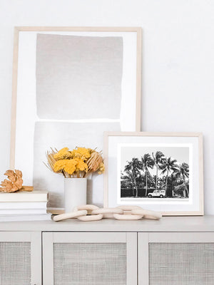 Black and white photo print of a vintage Land Rover Defender parked in front of palm trees in Palm Beach, Florida. Natural wood framed vintage Land Rover photo print paired with geometric art in a neutral, coastal casual living room with dried flowers and wood chain.. Land Rover photo print by Kristen M. Brown of Samba to the Sea, available at The Sunset Shop