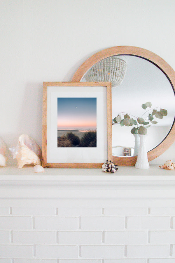 Full moon setting during a pastel pink sunrise on the Oregon Coast. "Pink Side of the Moon" sunrise beach print by Kristen M. Brown, Samba to the Sea. Coastal living framed Oregon Coast beach print shelfie on white fireplace mantle.