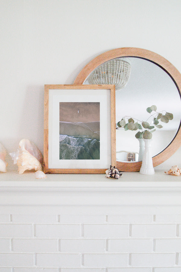 Aerial image of surfer on the beach in Nosara Costa Rica. Salt & Water aerial beach print photographed by Samba to the Sea for The Sunset Shop. Coastal living framed beach print shelfie on white fireplace mantle.