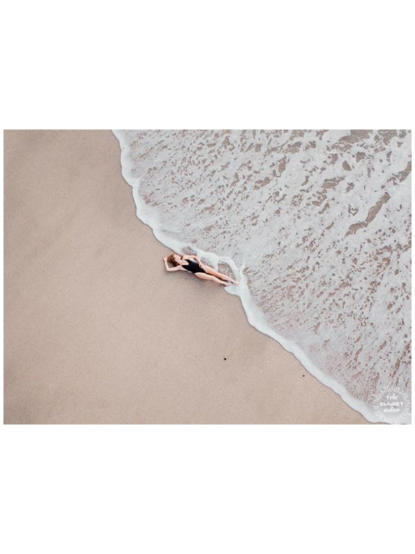 Woman laying on the beach as the waves reach her feet in Costa Rica. Photographed by Samba to the Sea for The Sunset Shop.