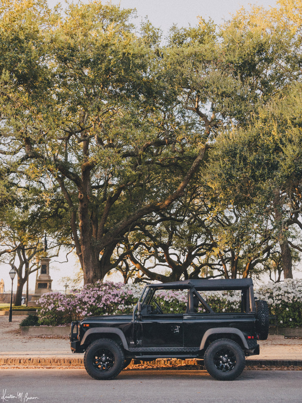 The early morning sun is just starting to stream through the Live Oak trees, the azaleas are in full bloom, and this D90 is waiting for you. Say hello to the intersection of classic Southern elegance and rugged adventure with this sleek Land Rover Defender ready for it&#39;s next adventure along Charleston&#39;s historic Battery. Photo print by Kristen M. Brown of Samba to the Sea for The Sunset Shop.