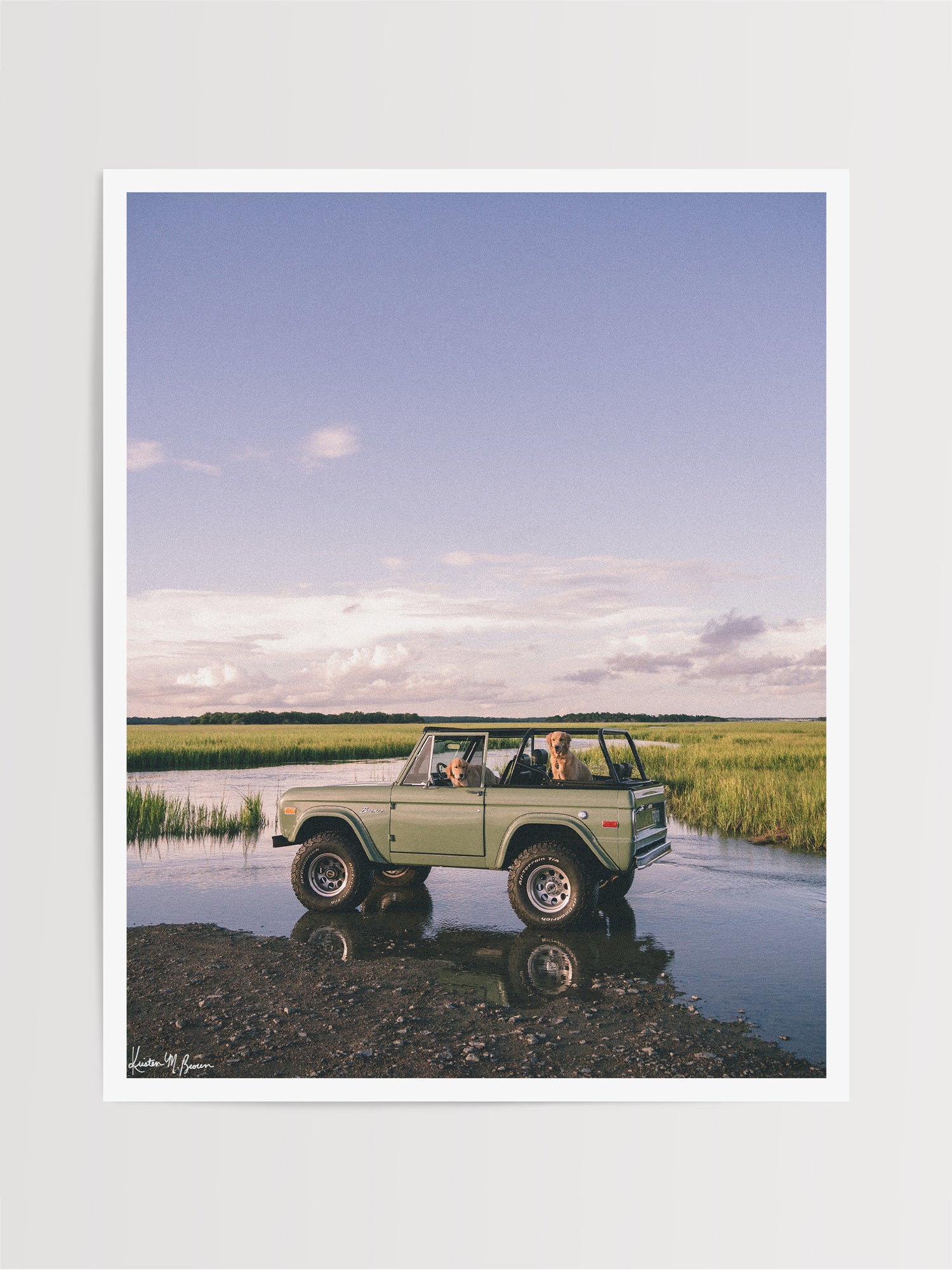 Photographic art print featuring a vintage green Ford Bronco along the marsh landscape under a pale blue sky with golden retrievers dogs waiting for an adventure. Lowcountry golden hours hit different when you’ve got four-wheel drive, a tailgate full of tail wags, and nowhere you’d rather be. "Best Friends and Bronco Rides" photo print of golden retrievers waiting for you to hop in a vintage Bronco to start the afternoon adventure along the marsh in Charleston, SC. Photograph by Kristen M. Brown.
