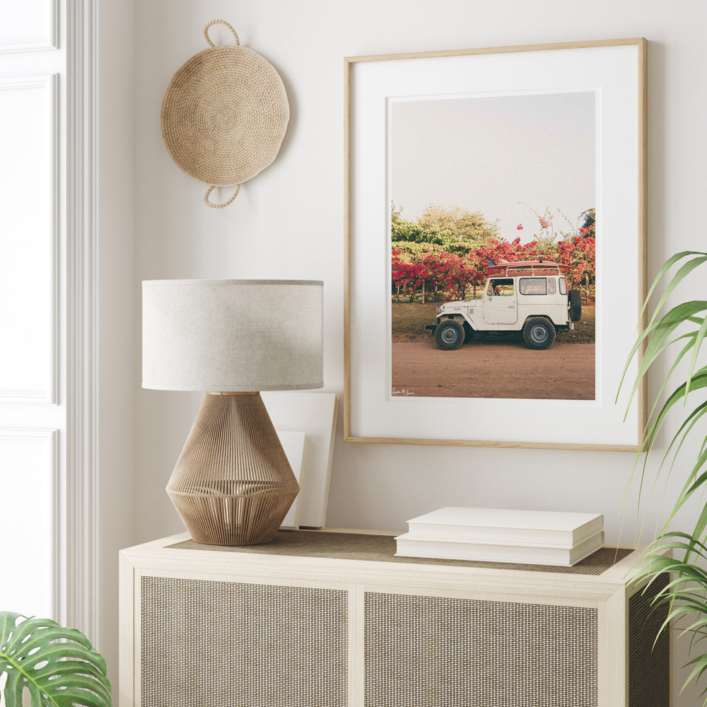 Tropical neutral room with palms, cane side table and vintage Land Cruiser and surfboards wall art. "Blooming and Cruising" photo print of vintage Toyota FJ40 Land Cruiser racked up with surfboards among vibrantly blooming Bougainvillea flowers in 