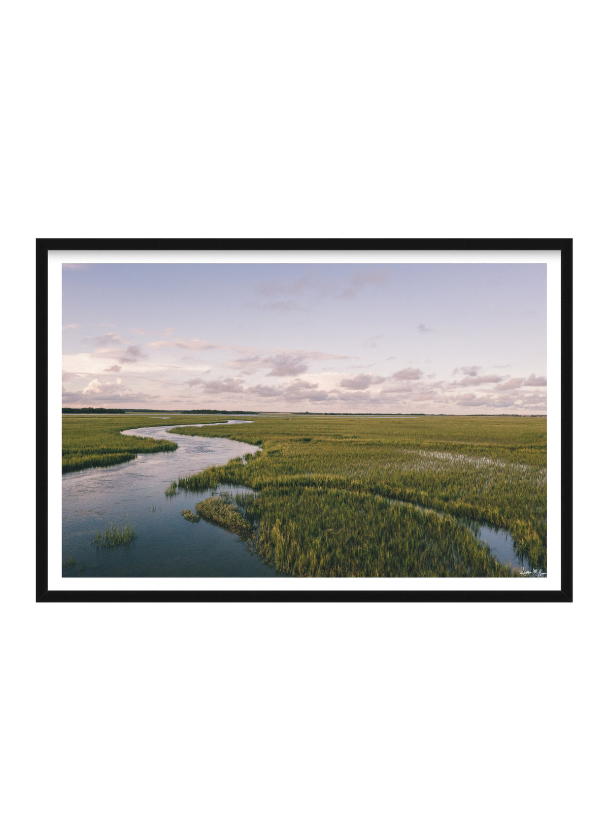 A framed landscape photograph of a winding river through a green marsh under a pale sky, presented in a black frame with a white mat on a white background.A scenic landscape photograph of a winding river flowing through a vast green marsh under a pale blue and pink sky. "Creek Serenade" photo print of golden hour over the a marsh wandering creek during high tide in Charleston, SC. Photo by Kristen M. Brown of Samba to the Sea for The Sunset Shop.