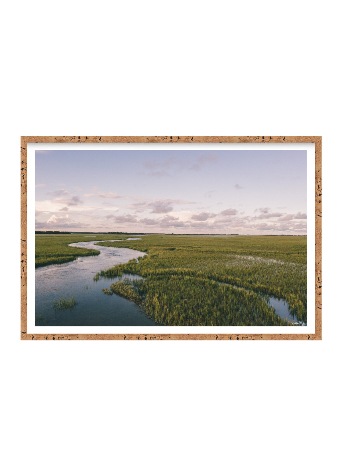 A framed landscape art print depicting a winding river through green marshlands under a pale sky, set in a cork frame with a white mat on a white background. A scenic landscape photograph of a winding river flowing through a vast green marsh under a pale blue and pink sky. "Creek Serenade" photo print of golden hour over the a marsh wandering creek during high tide in Charleston, SC. Photo by Kristen M. Brown of Samba to the Sea for The Sunset Shop.
