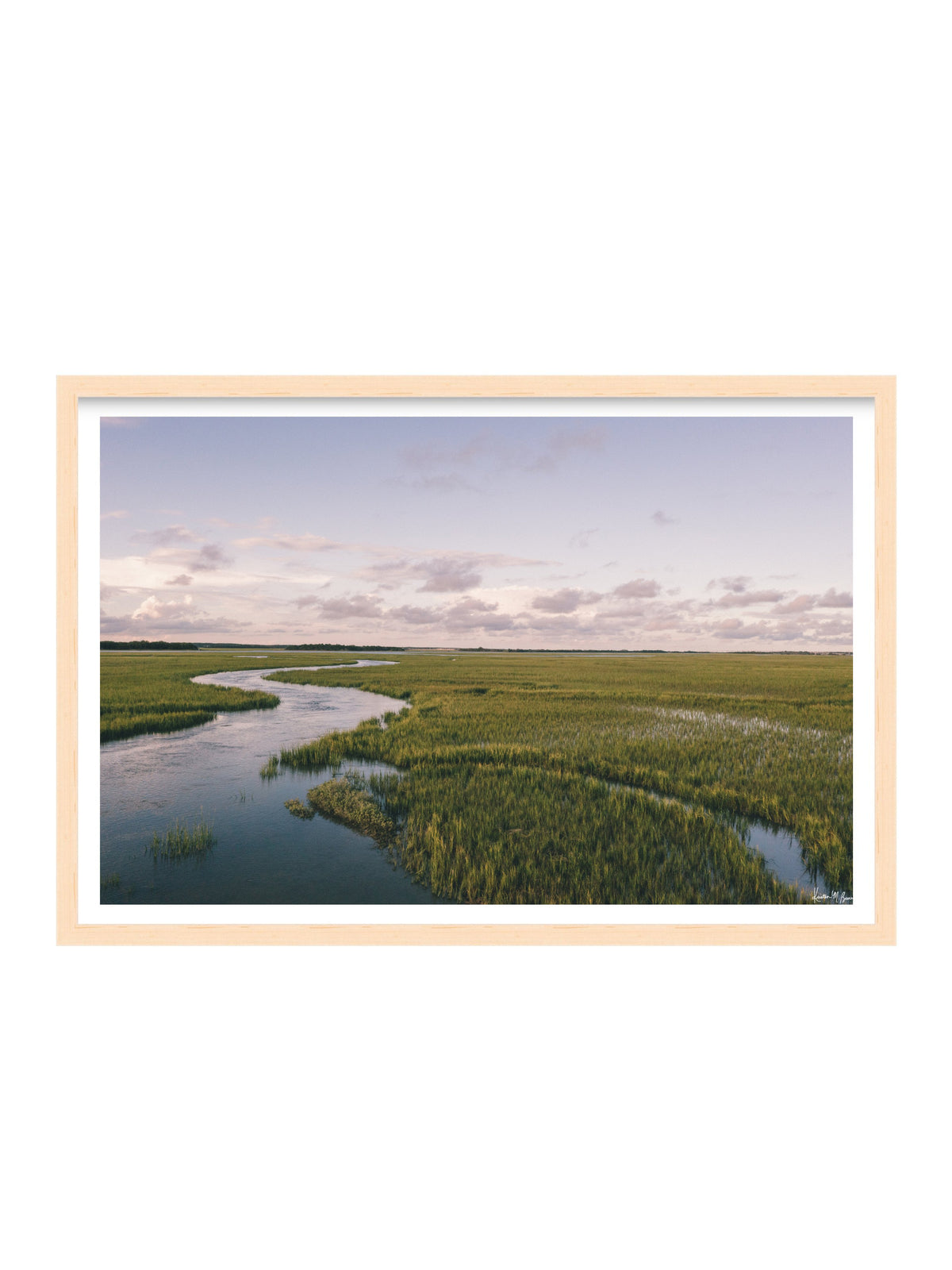 A framed landscape art print depicting a winding river through a green marsh under a cloudy sky, presented in a light wood frame with a white mat on a white background. A scenic landscape photograph of a winding river flowing through a vast green marsh under a pale blue and pink sky. "Creek Serenade" photo print of golden hour over the a marsh wandering creek during high tide in Charleston, SC. Photo by Kristen M. Brown of Samba to the Sea for The Sunset Shop.