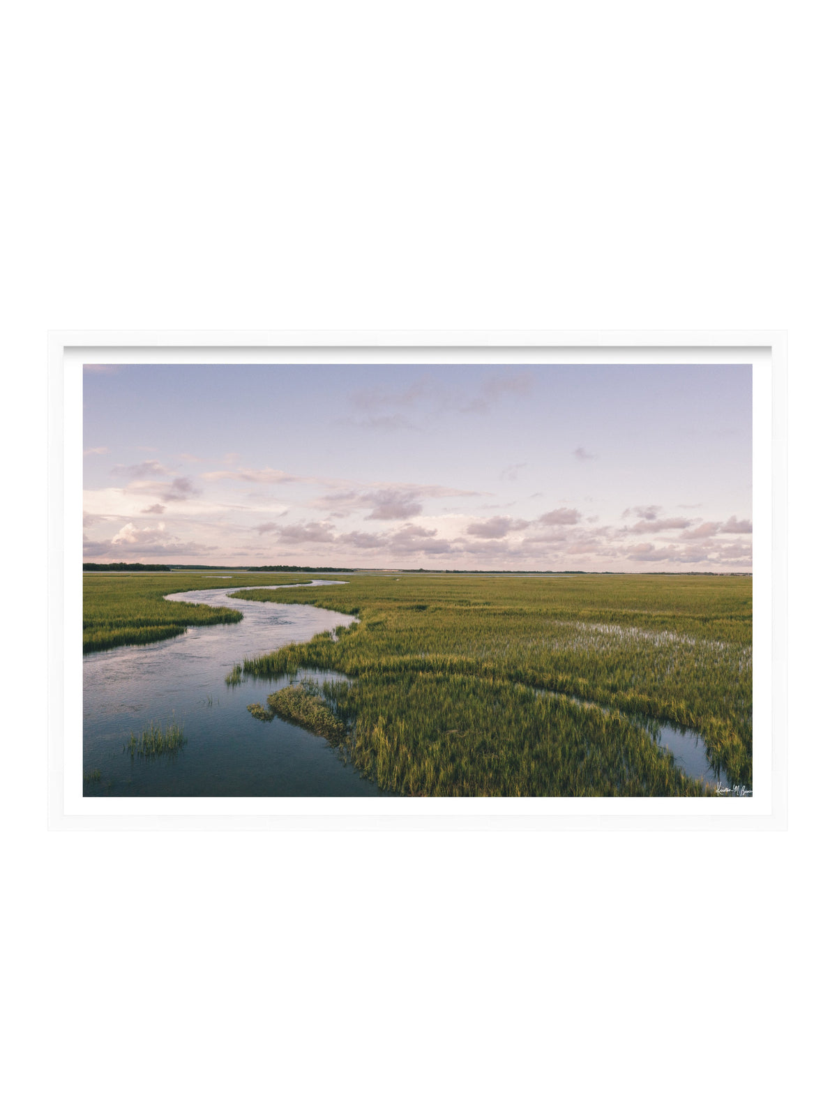 A framed landscape art print depicting a winding river through green marshlands under a pale sky, shown against a plain white background. A scenic landscape photograph of a winding river flowing through a vast green marsh under a pale blue and pink sky. "Creek Serenade" photo print of golden hour over the a marsh wandering creek during high tide in Charleston, SC. Photo by Kristen M. Brown of Samba to the Sea for The Sunset Shop.
