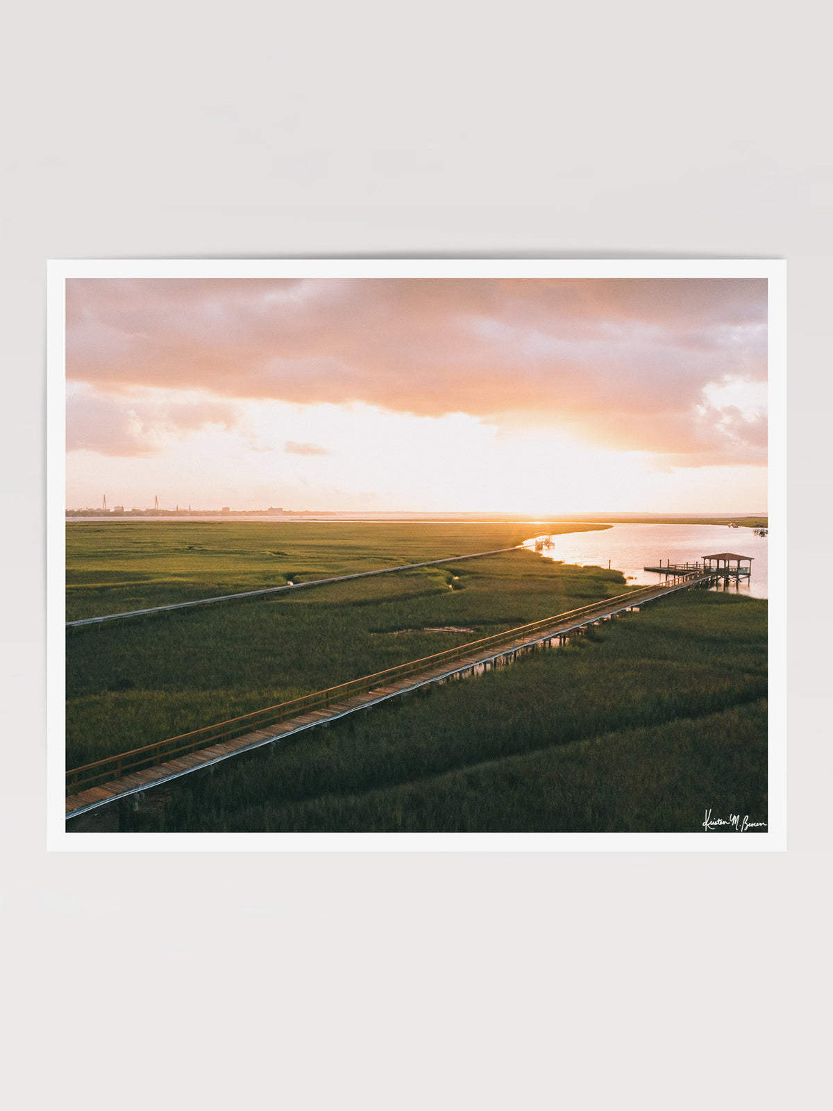 Aerial photograph of pastel pink sunrise over Charleston harbor and marsh with a boardwalk path, waterway, and view of downtown Charleston in the background. "Morning Harbor View" fine art photography print photographed by Kristen M. Brown, Samba to the Sea.
