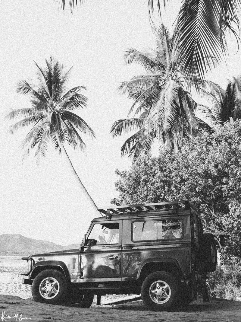 Nothing quite comes close to evoking that feeling that a tropical beach adventure is about to happen than a Land Rover Defender. So what are you waiting for? Hop on in and adventure away to find your tropical beach paradise! &quot;Paradise Found Rover&quot; black and white Land Rover Defender beach and palm trees photo print by Kristen M. Brown of Samba to the Sea for The Sunset Shop.