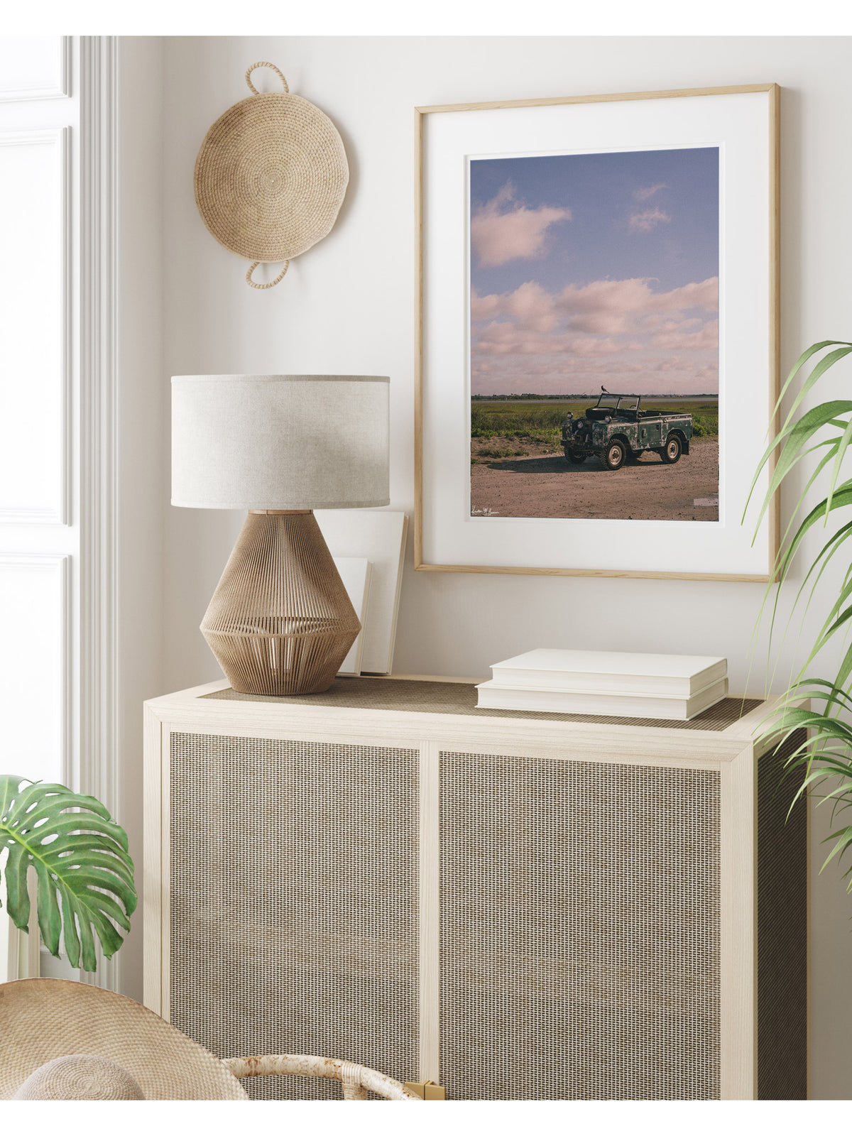 A framed art print featuring a vintage Land Rover series truck at the beach in Charleston, SC styled in a bright, modern room above a light wood cabinet with caning. Some stories aren’t written in books - they’re etched in weathered green paint, rusted edges, and decades of sand settled along coastal beach roads. Hop on in to "Perched Patrol" and bring home a piece of adventure. Vintage Land Rover photo print by Kristen M. Brown of the Sunset Shop.