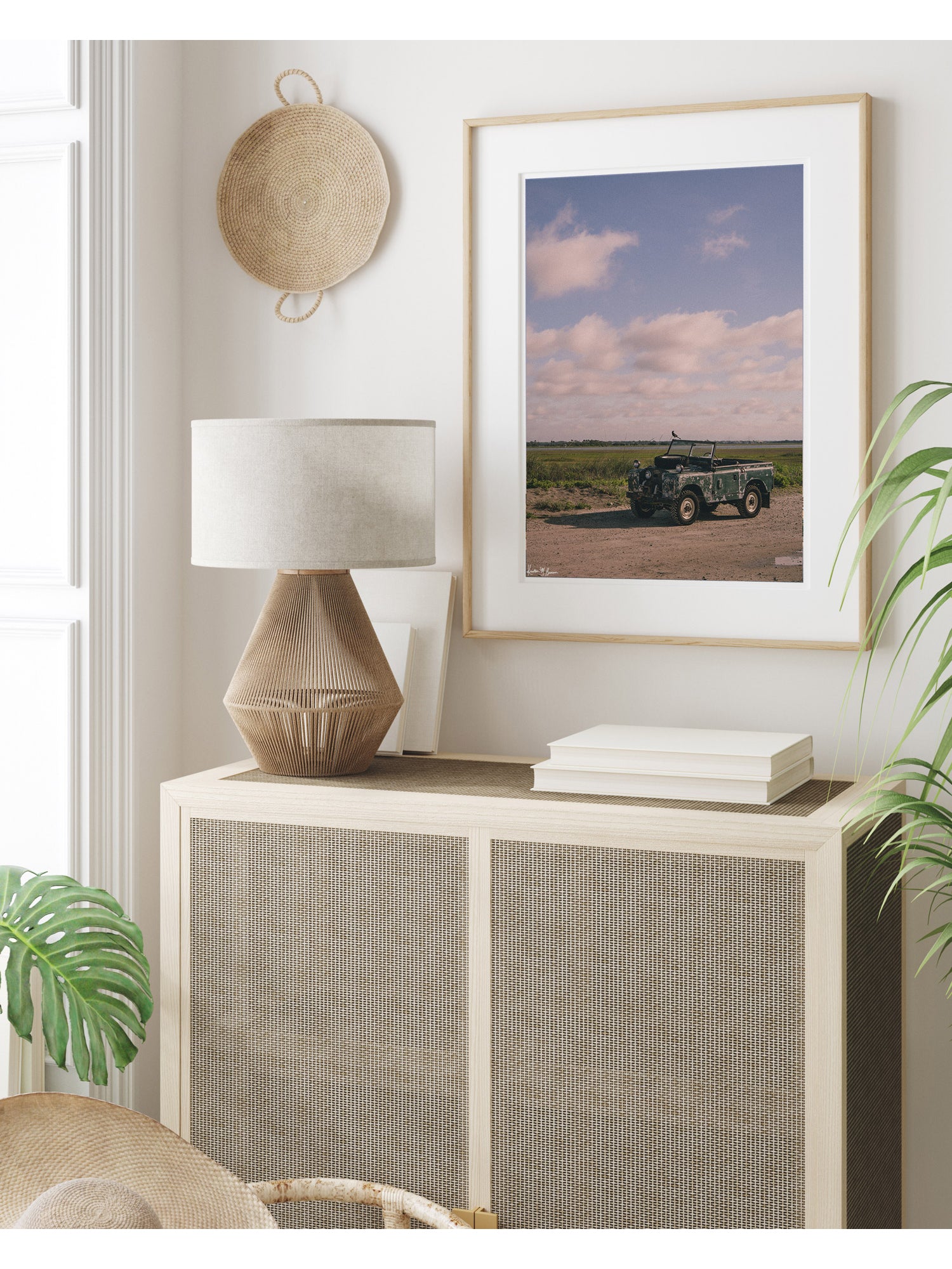 A framed art print featuring a vintage Land Rover series truck at the beach in Charleston, SC styled in a bright, modern room above a light wood cabinet with caning. Some stories aren’t written in books - they’re etched in weathered green paint, rusted edges, and decades of sand settled along coastal beach roads. Hop on in to "Perched Patrol" and bring home a piece of adventure. Vintage Land Rover photo print by Kristen M. Brown of the Sunset Shop.