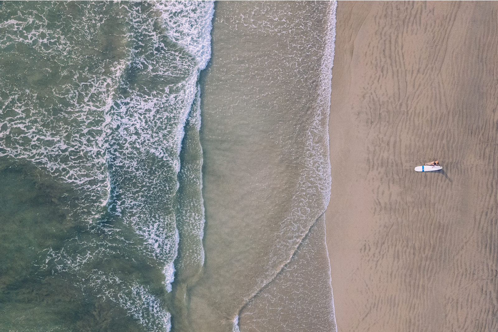 Aerial image of surfer girl sitting on the beach in Playa Guiones / Nosara, Costa Rica. Photographed by Kristen M. Brown of Samba to the Sea.