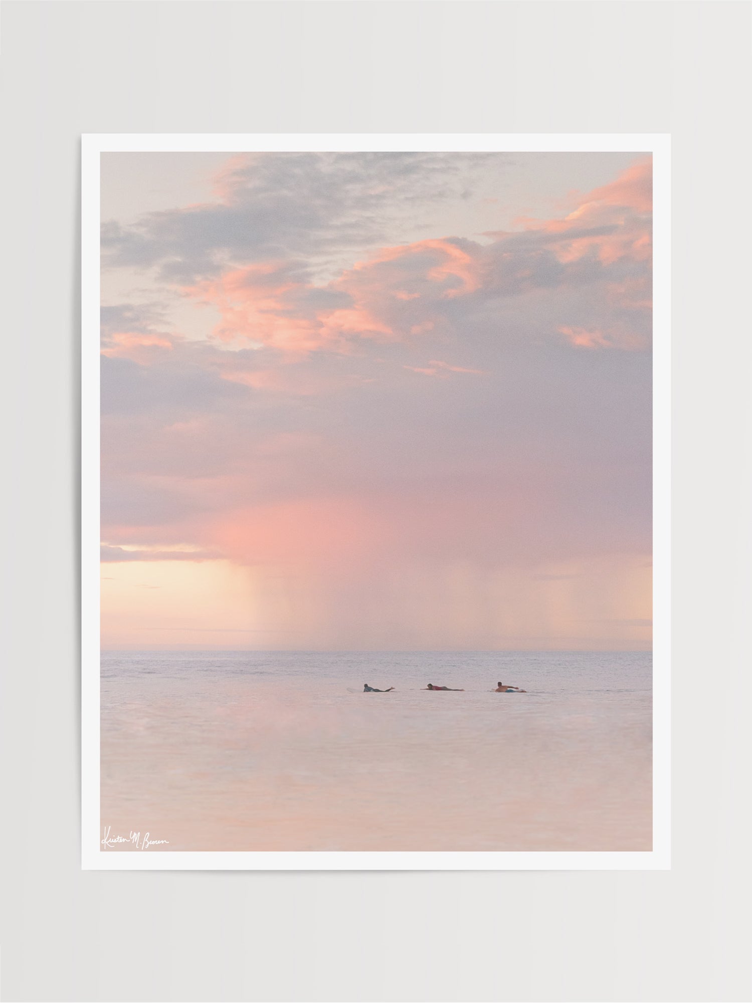 Surfers paddling in the ocean during a pastel pink rain squall at sunset in Costa Rica. What a surfer's dreams are made of - - beautiful sunset surf sessions. Have a piece of sunset surfer magic in your very own home with "Saltwater Paradise" sunset surfer wall art photographed by Kristen M. Brown of Samba to the Sea for The Sunset Shop.