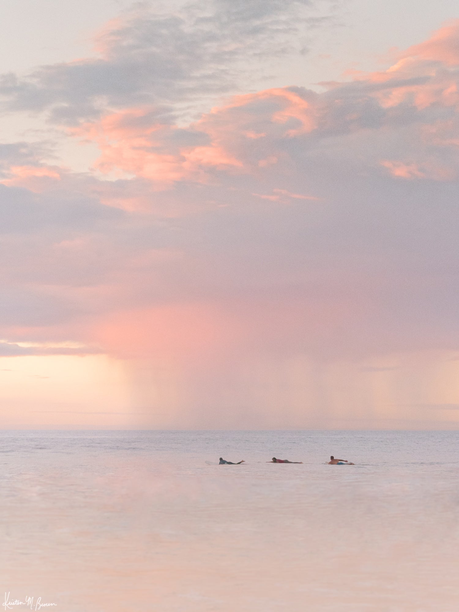 Surfers paddling in the ocean during a pastel pink rain squall at sunset in Costa Rica. What a surfer's dreams are made of - - beautiful sunset surf sessions. Have a piece of sunset surfer magic in your very own home with "Saltwater Paradise" sunset surfer wall art photographed by Kristen M. Brown of Samba to the Sea for The Sunset Shop.