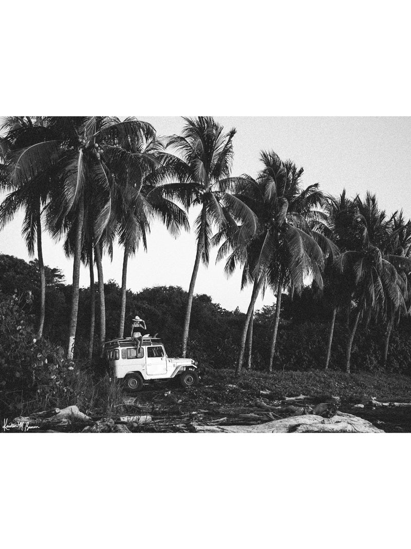 "Surf Bandida" black and white photo print of surfer girl checking the surf with her vintage Toyota FJ40 Land Cruiser racked up with surfboards among the palm trees in Costa Rica. Photographed by Costa Rica photographer Kristen M. Brown of Samba to the Sea for The Sunset Shop.