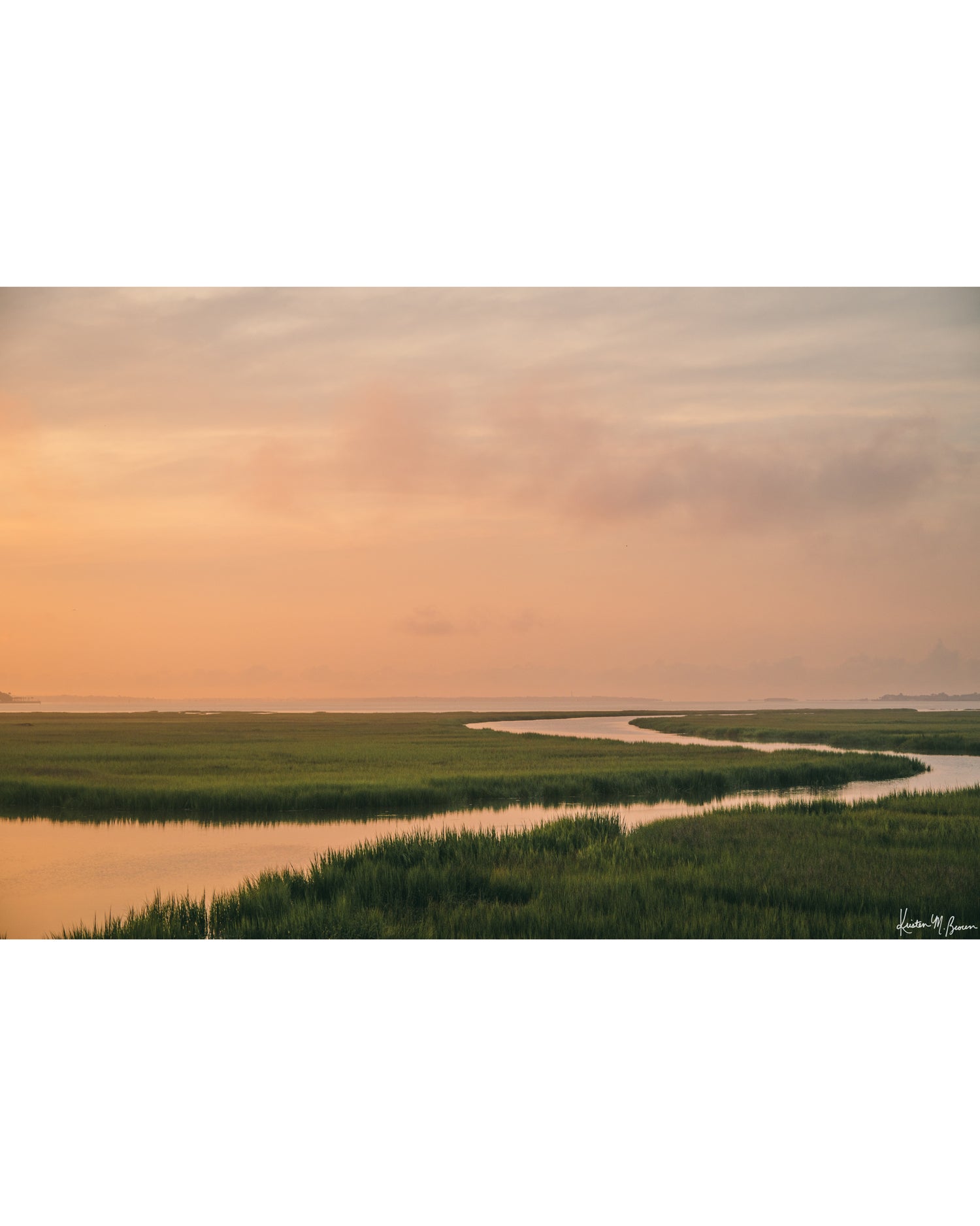 A scenic landscape photograph of a winding creek flowing through the marsh during sunrise, with the soft peach and pink clouds in the sky above and reflecting in the waters. "Tidal Glow" fine art photography print photographed by Kristen M. Brown, Samba to the Sea.
