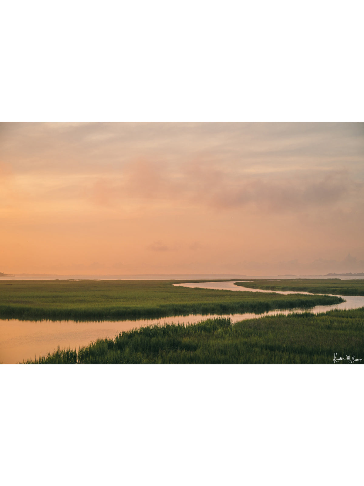 A scenic landscape photograph of a winding creek flowing through the marsh during sunrise, with the soft peach and pink clouds in the sky above and reflecting in the waters. "Tidal Glow" fine art photography print photographed by Kristen M. Brown, Samba to the Sea.