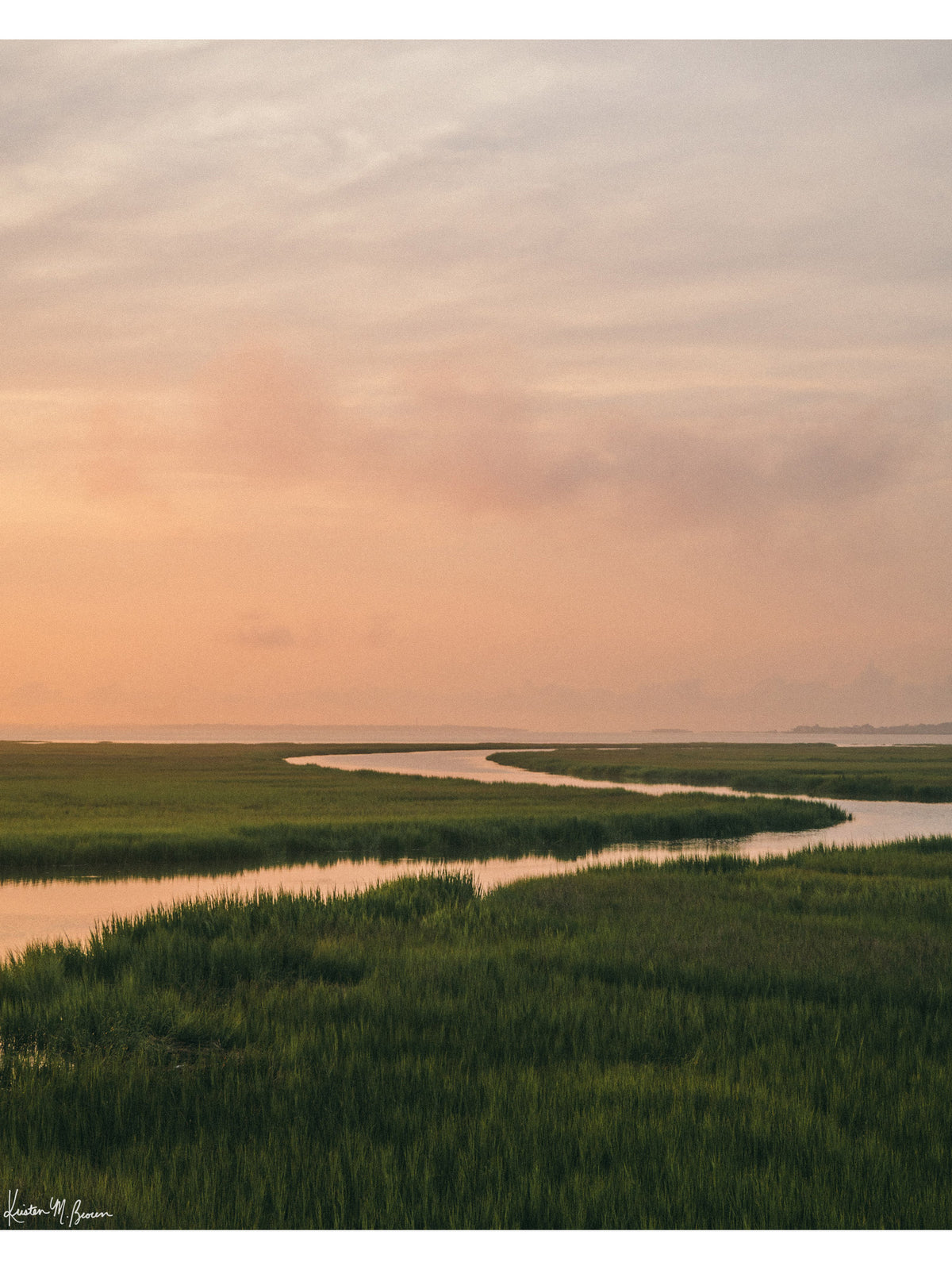 A scenic landscape photograph of a winding creek flowing through the marsh during sunrise, with the soft peach and pink clouds in the sky above and reflecting in the waters. "Tidal Glow" fine art photography print photographed by Kristen M. Brown, Samba to the Sea.