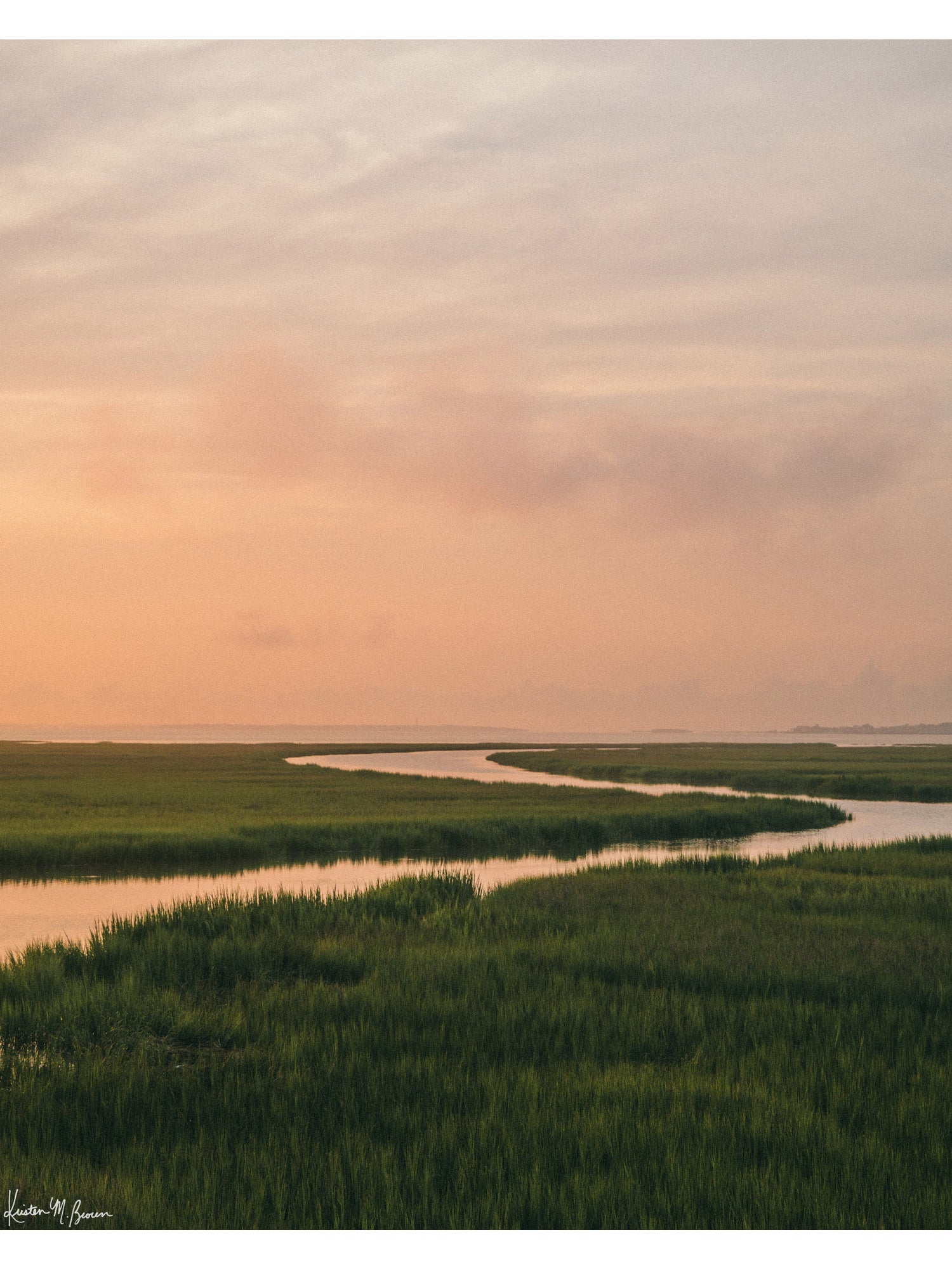 A scenic landscape photograph of a winding creek flowing through the marsh during sunrise, with the soft peach and pink clouds in the sky above and reflecting in the waters. "Tidal Glow" fine art photography print photographed by Kristen M. Brown, Samba to the Sea.