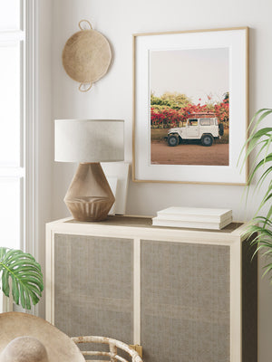 Tropical neutral room with palms, cane side table and vintage Land Cruiser and surfboards wall art. "Blooming and Cruising" photo print of vintage Toyota FJ40 Land Cruiser racked up with surfboards among vibrantly blooming Bougainvillea flowers in Costa Rica. Photographed by Costa Rica photographer Kristen M. Brown of Samba to the Sea for The Sunset Shop.