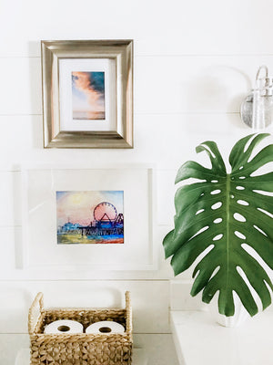Beautiful shiplap white coastal bathroom with a breathtaking sunset print by Samba to the Sea and watercolor painting.