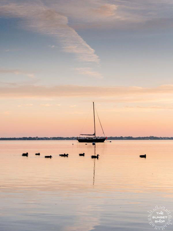Take a deep breath and welcome a beautiful new day with a serene sunrise sky over the bay. Sunrise image of ducks swimming past a sailboat in the bay in Huntington, NY. Photographed by Kristen M. Brown, Samba to the Sea.