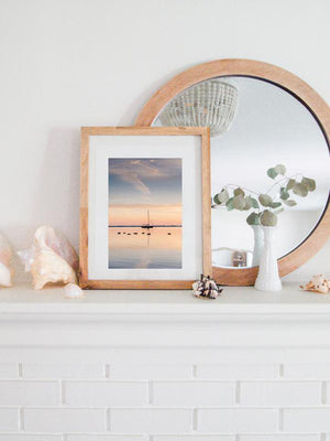 Take a deep breath and welcome a beautiful new day with a serene sunrise sky over the bay. Sunrise image of ducks swimming past a sailboat in the bay in Huntington, NY. Photographed by Kristen M. Brown, Samba to the Sea. Coastal living framed sunrise coastal print shelfie on white fireplace mantle.