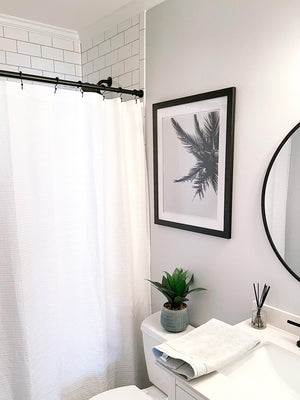 Black and white palm tree photo print hanging in modern farmhouse bathroom with white subway tile and black hardware. "Find Me Under the Palms" black and white palm tree print by Kristen M. Brown of Samba to the Sea for The Sunset Shop.
