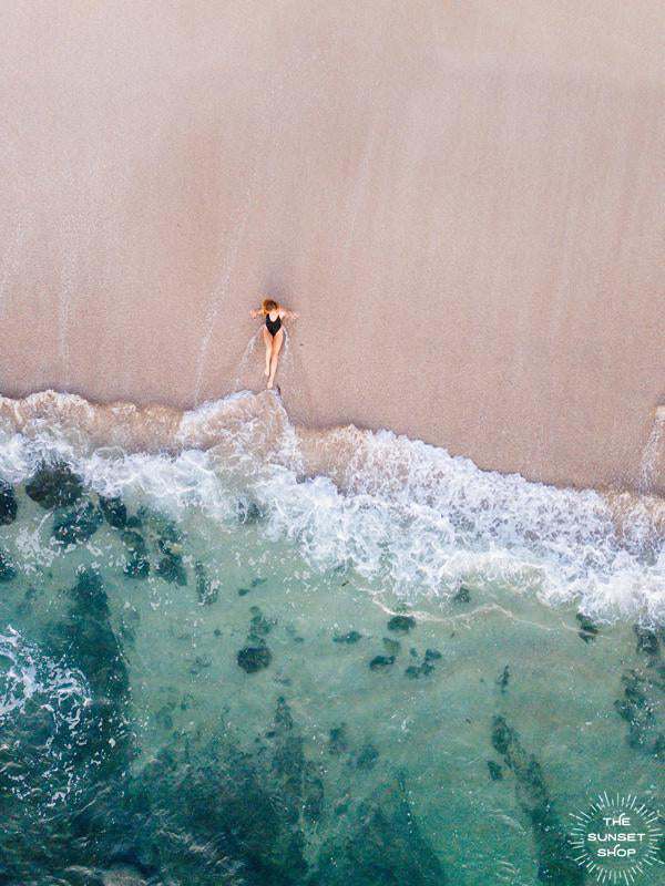 Woman laying on the beach as the waves reach her feet in Costa Rica. Photographed by Samba to the Sea for The Sunset Shop. 