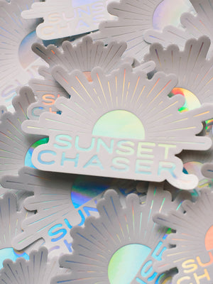Do you love to chase sunsets? Is sunset your favorite color? Then this Sunset Chaser holographic sticker has your name on it!  Printed with a holographic sheen, you'll be mesmerized by how this sticker changes colors as it catches and reflects light -- just like breathtaking sunset! From shades of ocean turquoise to pink sunset, this Sunset Chaser sticker is your little slice of sunset magic. By Samba to the Sea at The Sunset Shop.