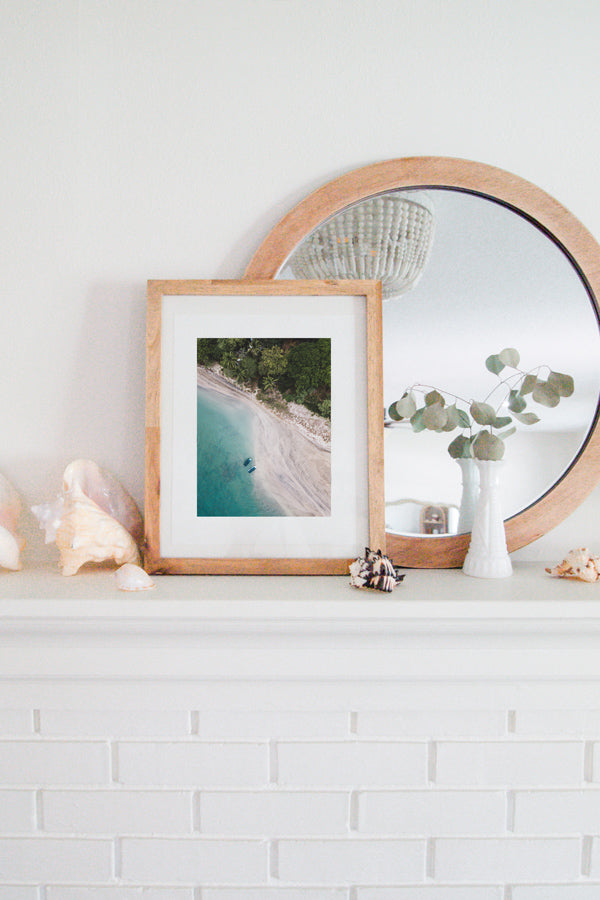 Tamarindo Costa Rica estuary. Aerial image of turquoise water, white sand beach, boats, and palm trees. Aerial beach print by Samba to the Sea at The Sunset Shop. Coastal living framed beach print shelfie on white fireplace mantle.