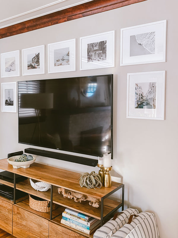 Black and white gallery wall above tv. Restored craftsman home in Ohio. Gallery image featuring "Let's Go to the Beach / Vamos a la Playa" black and white aerial beach sunbather image photographed by Kristen M. Brown of Samba to the Sea for The Sunset Shop.