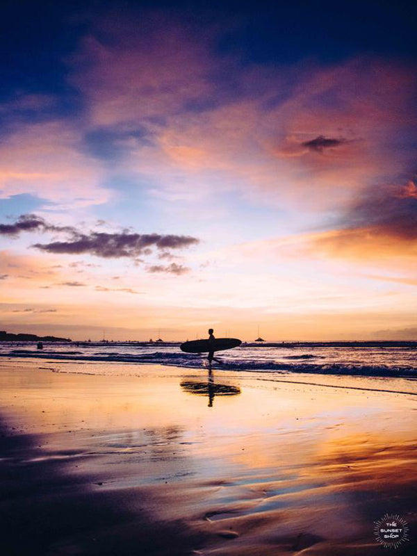 "Live Like a Local" sunset surfer print by Samba to the Sea at The Sunset Shop. Image of a surfer walking on the beach during a magical sunset in Tamarindo, Costa Rica.