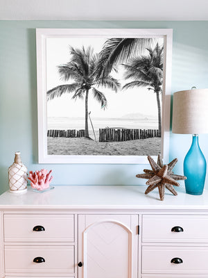 Coastal living bedroom with black and white photo print.Instantly transport yourself to your surf paradise with this black and white image of your surfboards - your magic sticks - patiently waiting under palm trees for you and your surf amigo/a to paddle out! Black and white image of two Robert August surfboards waiting to paddle out while laying under palm trees in Costa Rica. "Magic Sticks" palm tree surf print photographed by Kristen M. Brown of Samba to the Sea for The Sunset Shop.