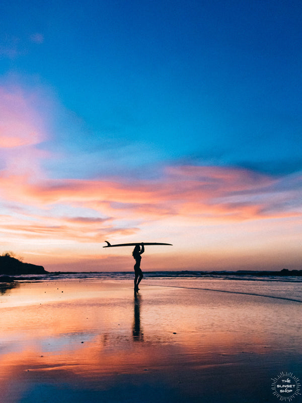 Pura Amor / Pure Love sunset female surfer print by Samba to the Sea at The Sunset Shop. Photo of a female surfer on the beach during a breathtaking sunset in Tamarindo, Costa Rica.