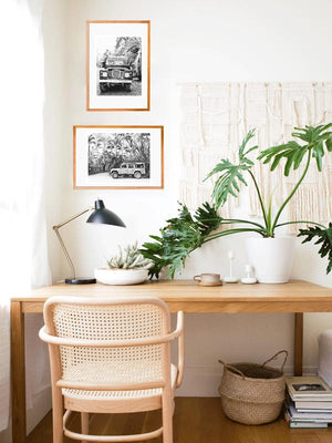 Black and white Land Rover photo prints hanging in a boho work from home desk area with hanging macrame, philodendron plant, mini cactus, cane desk chair, and belly basket. Land Rover prints available at The Sunset Shop by Samba to the Sea.