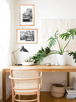 Black and white Land Rover photo prints hanging in a boho work from home desk area with hanging macrame, philodendron plant, mini cactus, cane desk chair, and belly basket. Land Rover prints available at The Sunset Shop by Samba to the Sea.