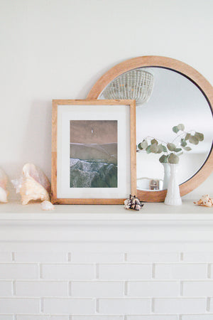 Aerial image of surfer on the beach in Nosara Costa Rica. Salt & Water aerial beach print photographed by Samba to the Sea for The Sunset Shop. Coastal living framed beach print shelfie on white fireplace mantle. 