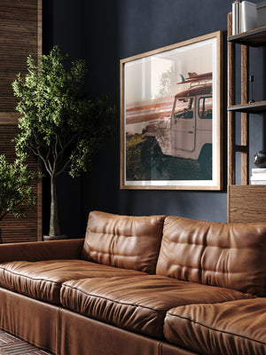 Vintage Land Cruiser and surfboards wall art in man cave library with dark walls and leather couch.