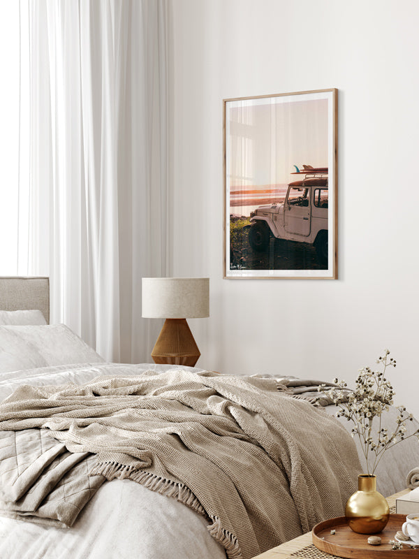 Surf photography vintage Land Cruiser wall art in neutral bedroom with caning furniture. "Seek and You Will Find" photo print of vintage Toyota FJ40 Land Cruiser racked up with surfboards parked at the beach in Costa Rica as the waves peel and the sun kissing the horizon turns everything golden. Photographed by Costa Rica photographer Kristen M. Brown of Samba to the Sea for The Sunset Shop.