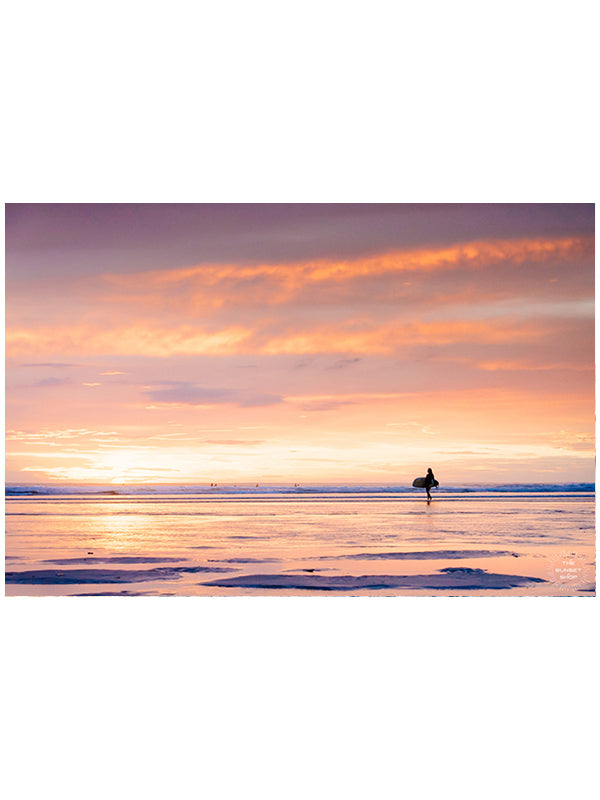 She&#39;s Magic sunset surfer print by Samba to the Sea at The Sunset Shop. Photo of a female surfer walking on the beach during a pastel pink sunset in Tamarindo, Costa Rica.