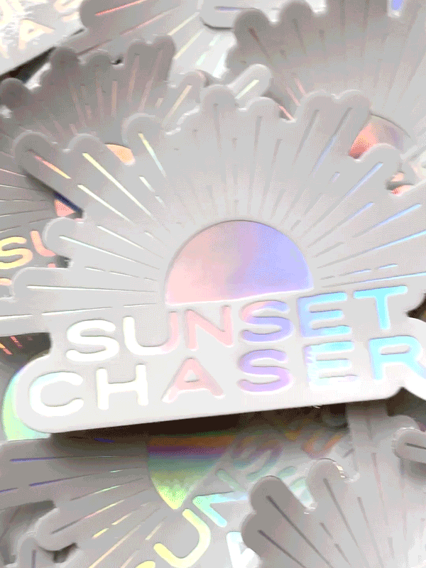 Do you love to chase sunsets? Is sunset your favorite color? Then this Sunset Chaser holographic sticker has your name on it!  Printed with a holographic sheen, you'll be mesmerized by how this sticker changes colors as it catches and reflects light -- just like breathtaking sunset! From shades of ocean turquoise to pink sunset, this Sunset Chaser sticker is your little slice of sunset magic. By Samba to the Sea at The Sunset Shop.